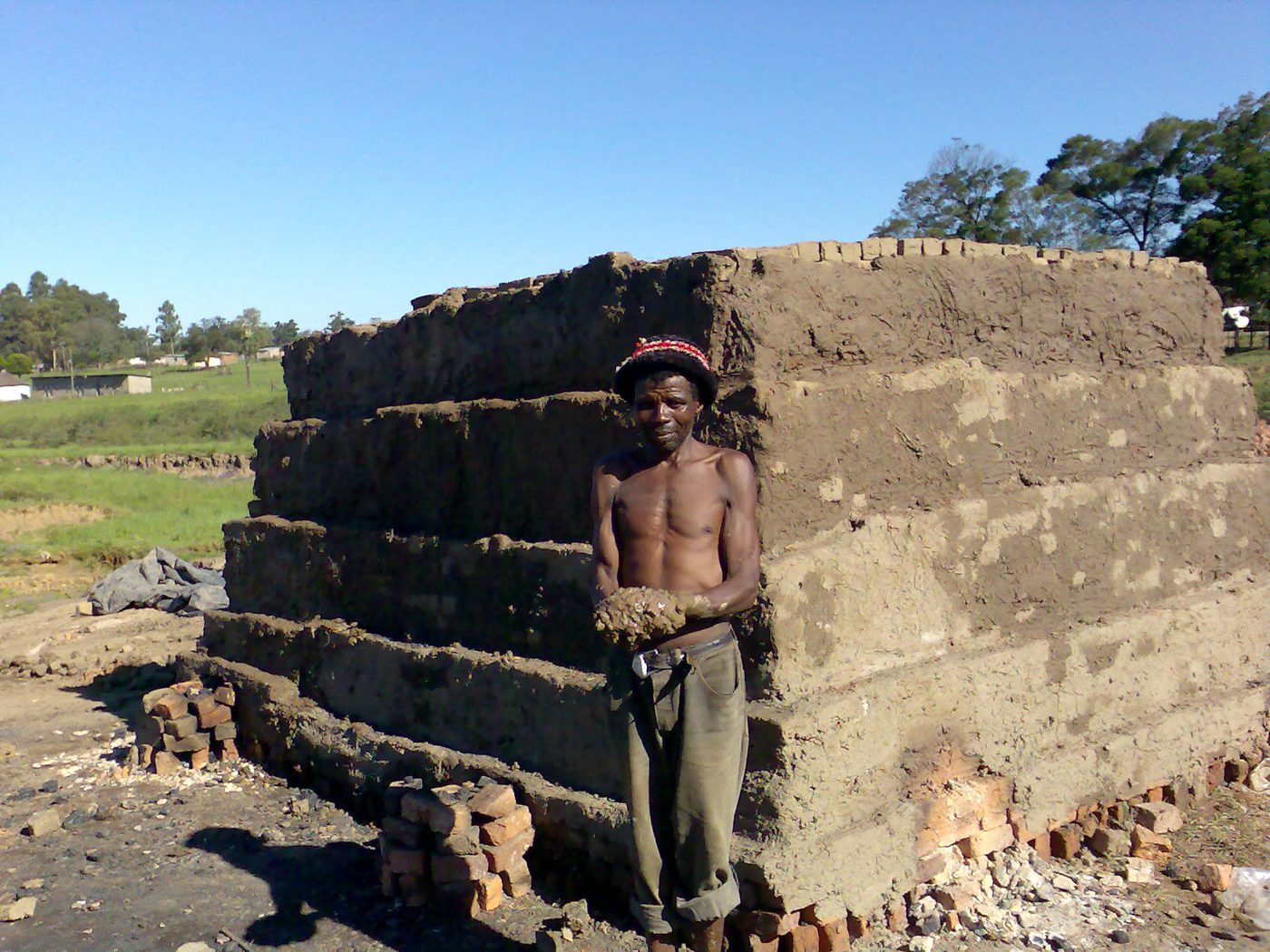A brickmaker beside a stacked clamp kiln of green clay bricks
