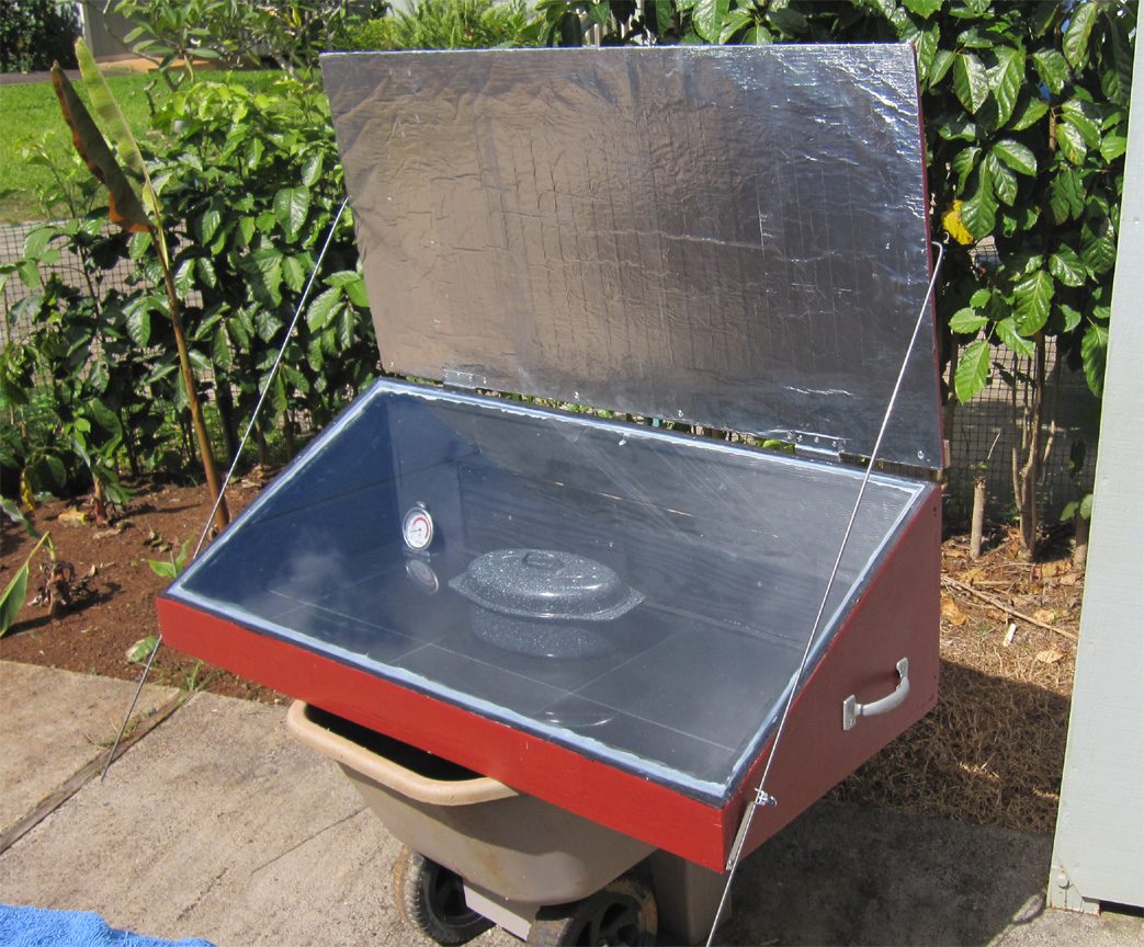 A plywood solar box cooker with glazed lid and reflector, pot inside on a dark absorber plate