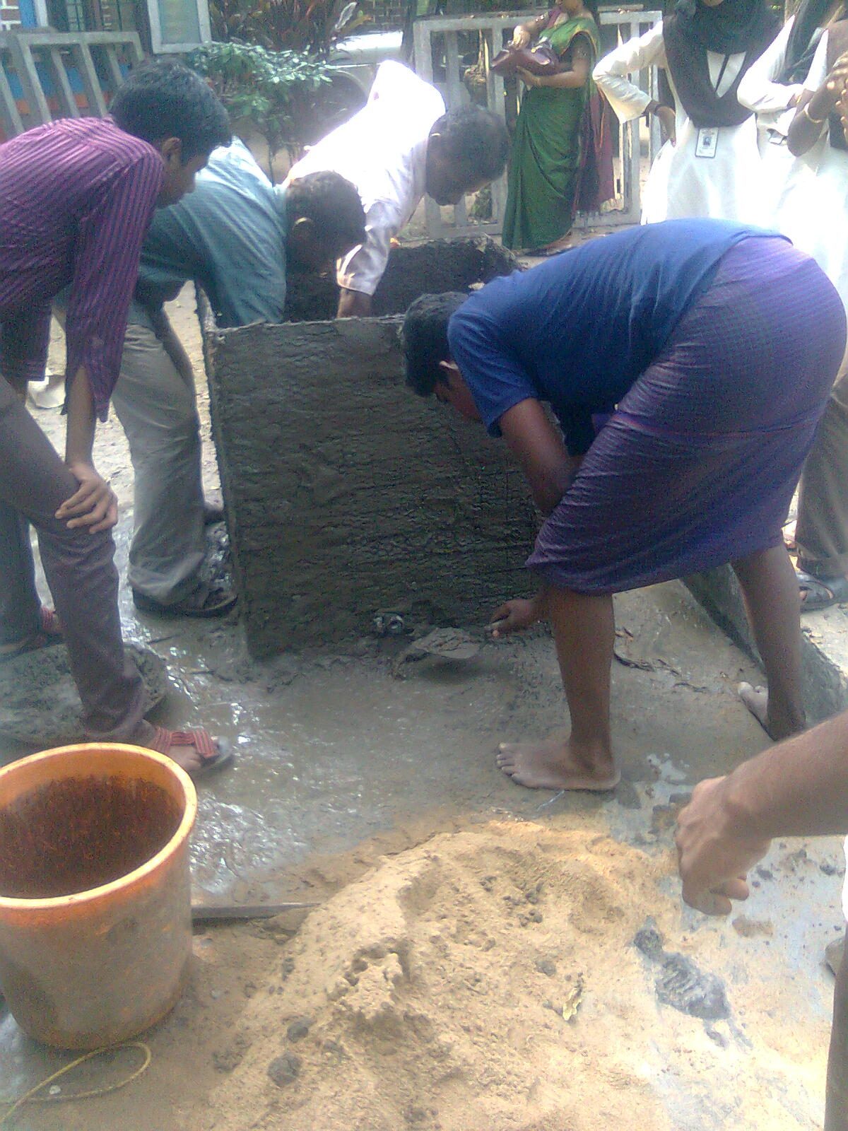 Workers plastering mortar onto the chicken-mesh shell of a ferrocement water tank