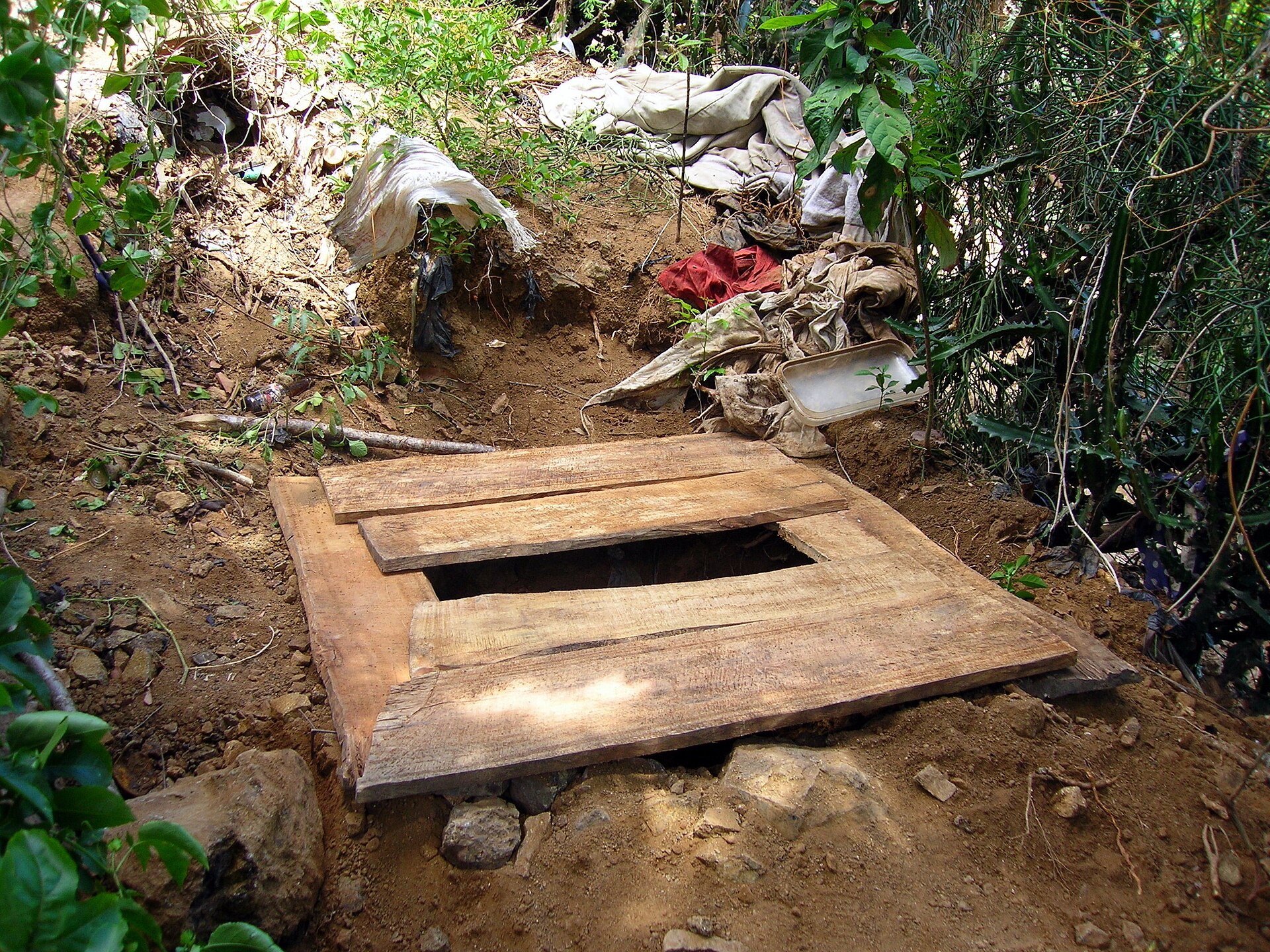 A timber platform with a squat opening laid over a shallow arborloo pit, the low-cost alternative to a cast concrete slab