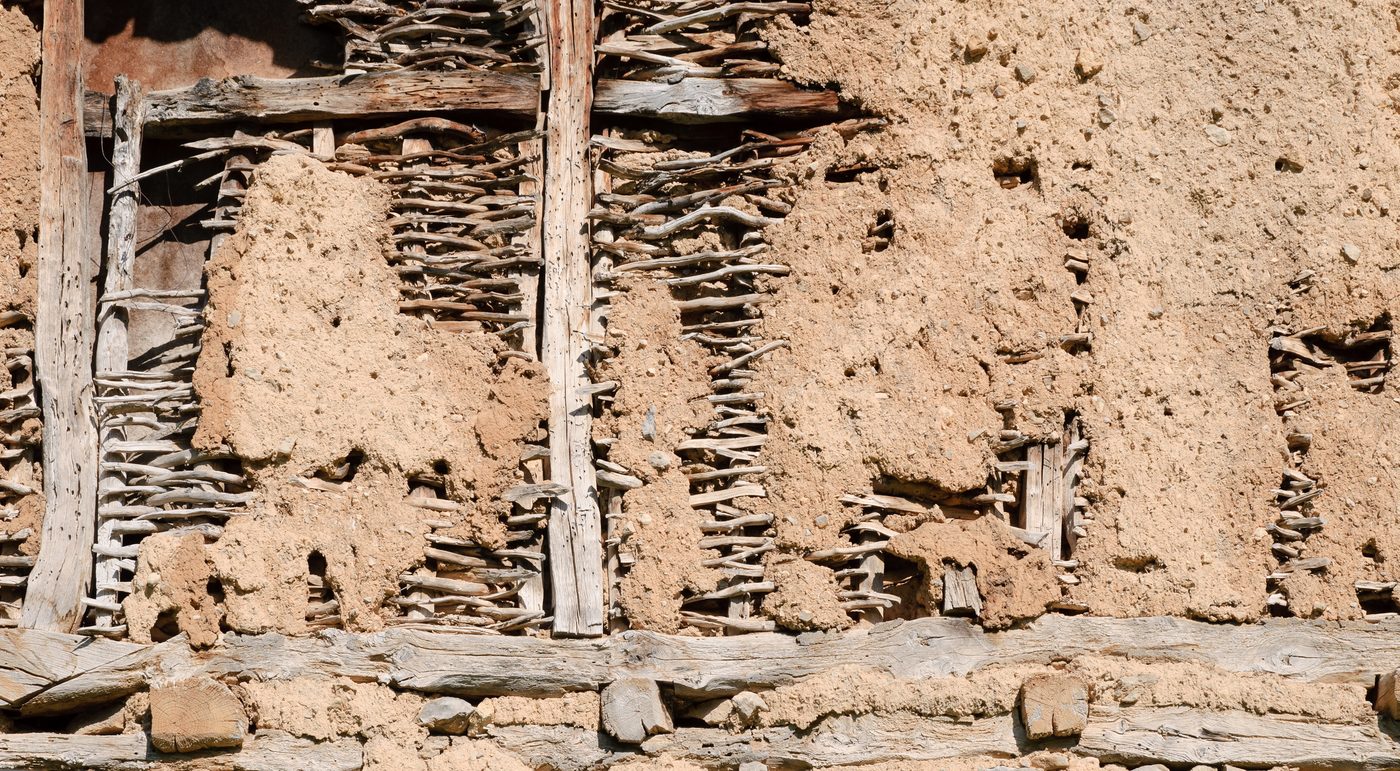 A woven lattice of poles being packed with clay daub to form a wall