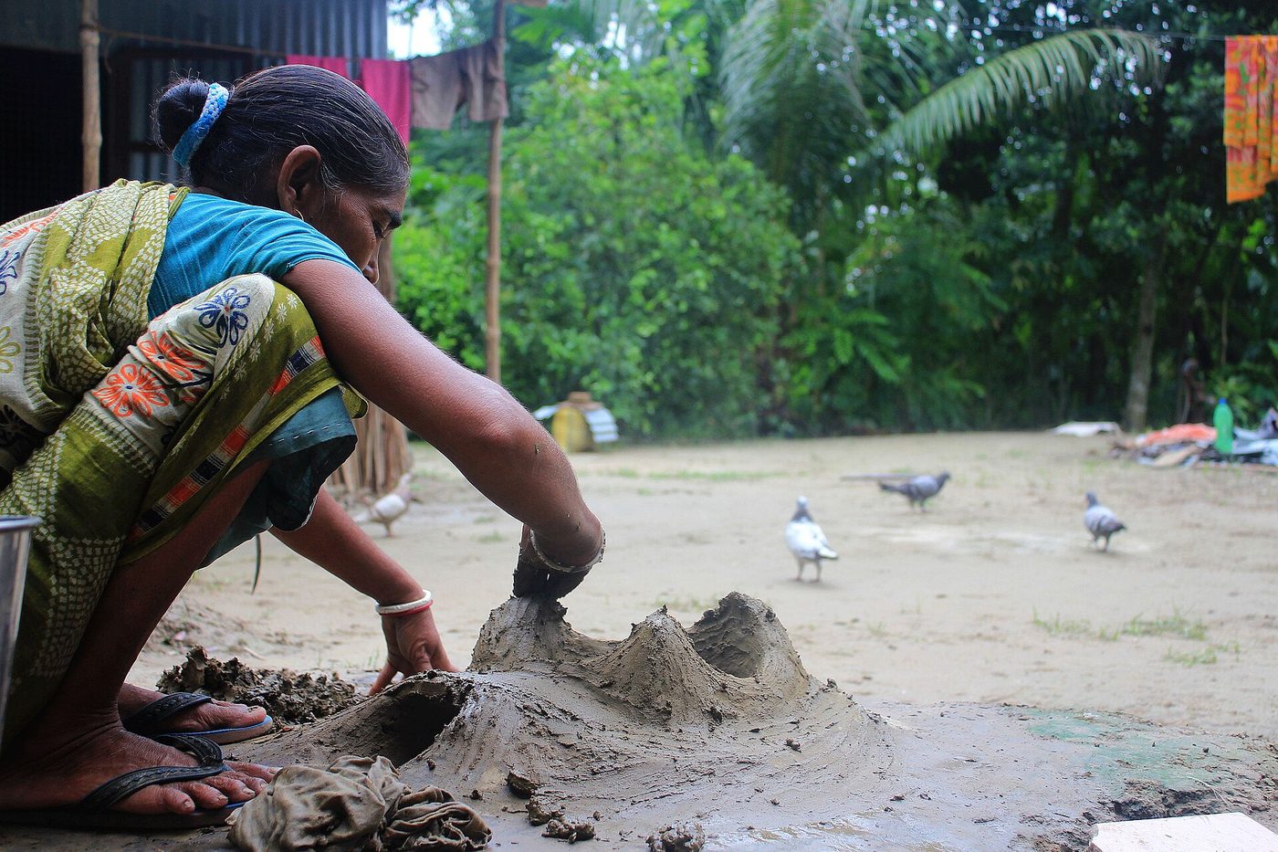A builder shaping the clay dome of an earth oven by hand on a prepared base