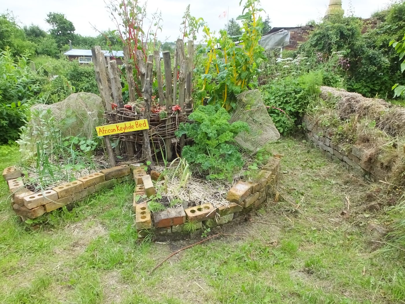 African-style keyhole garden bed built from stone and timber with a central compost basket