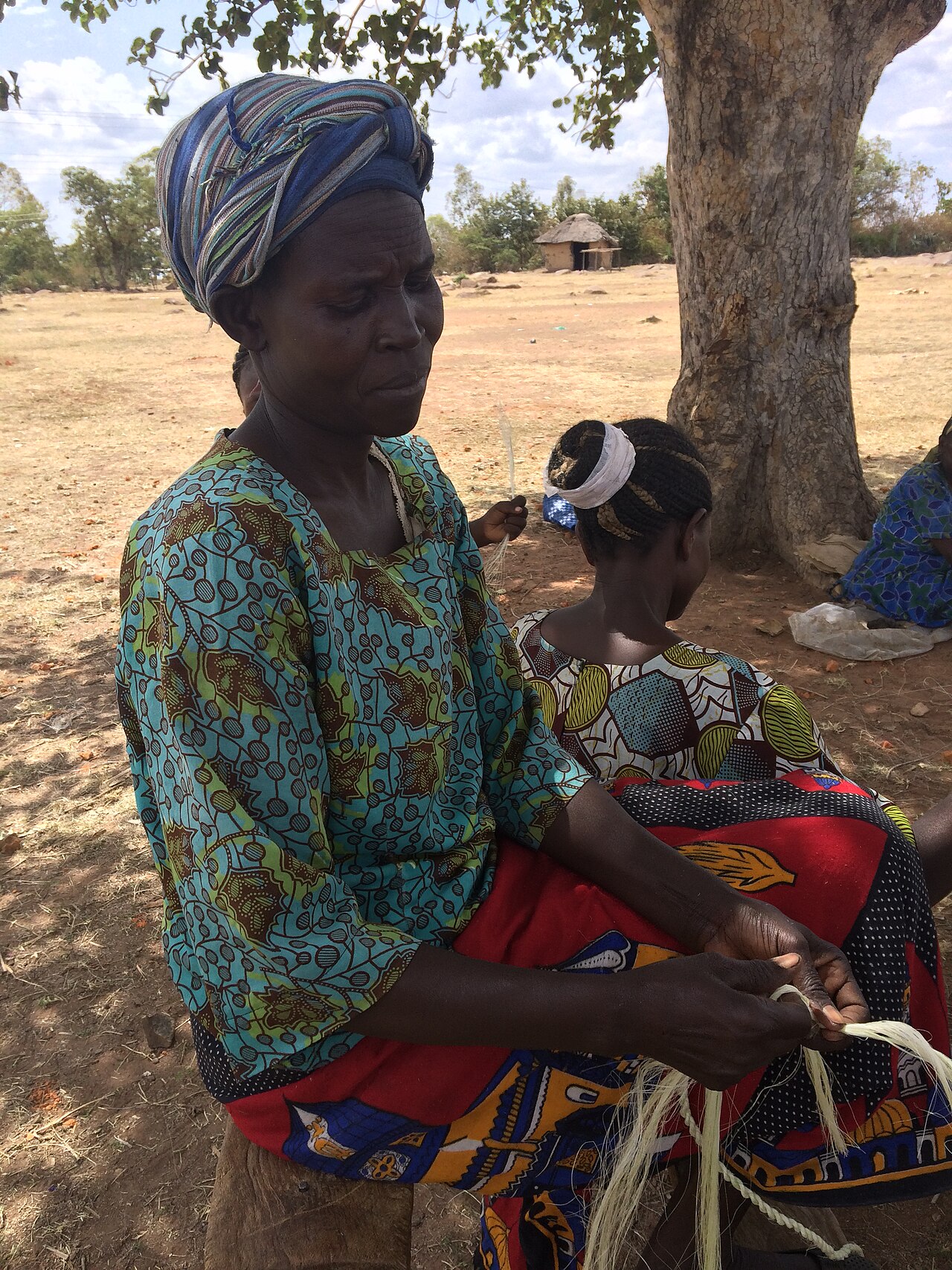 Women of the Ochuna craft cooperative in Kenya twisting sisal fibre into rope by hand under a tree