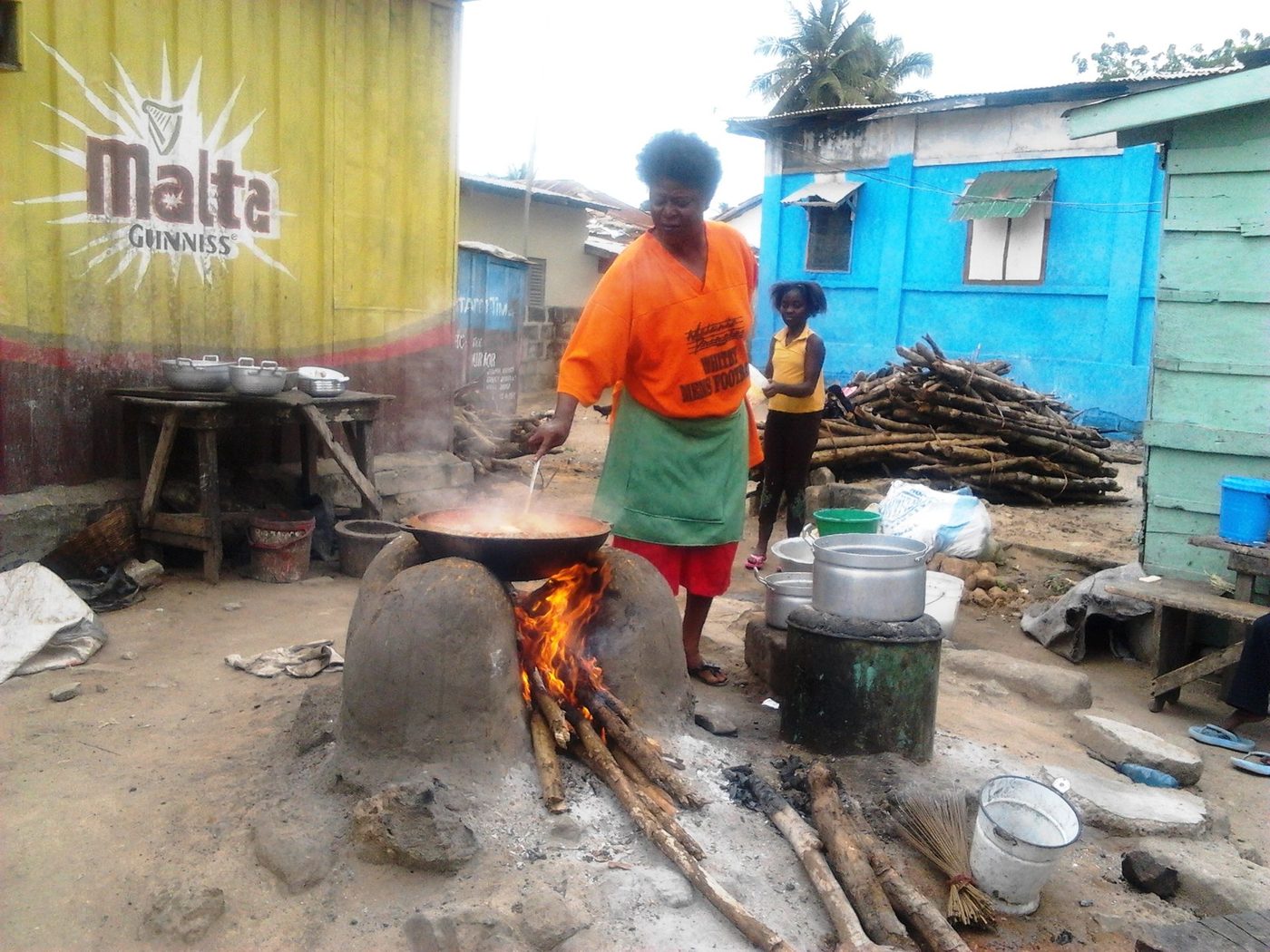 A cook working over a moulded mud stove with a pot seated in the stove opening