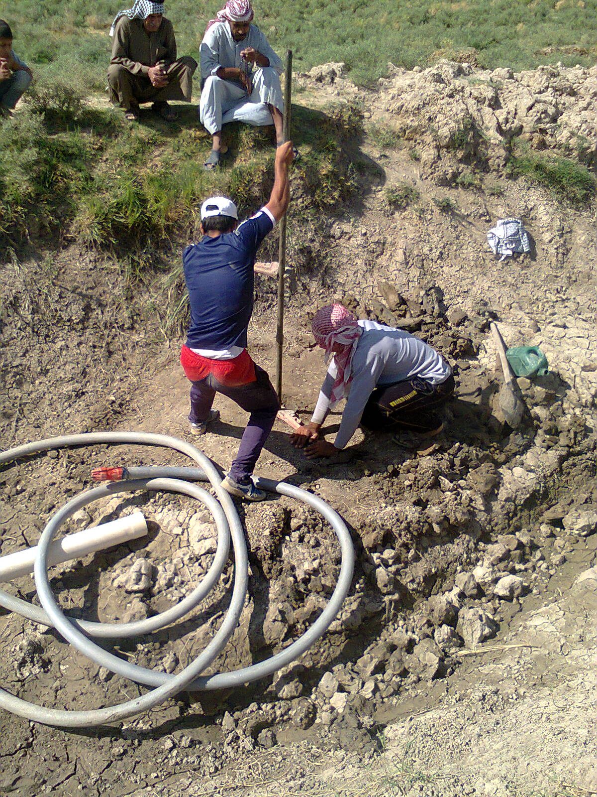 A crew hand-drilling a shallow well with auger rods turned by a T-handle